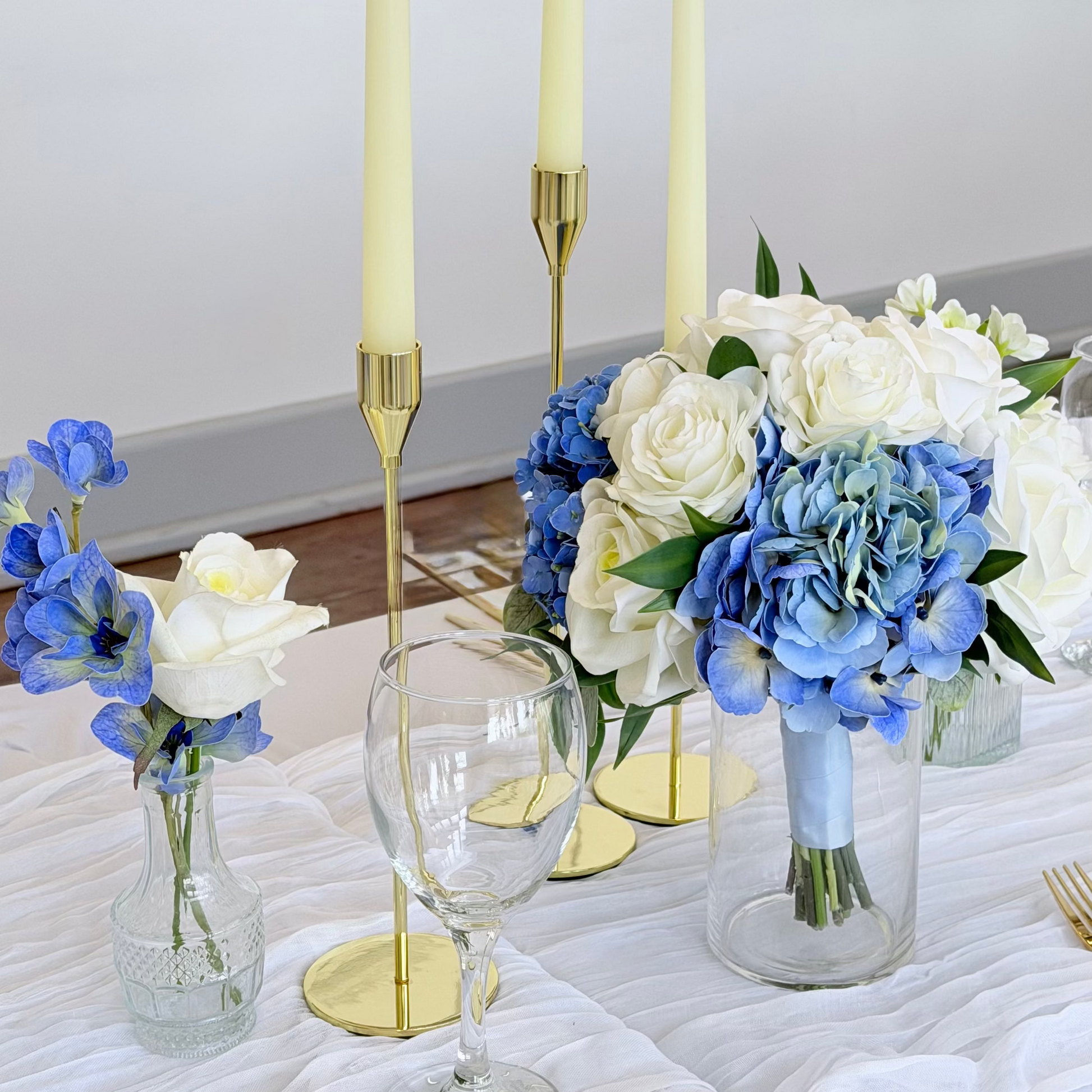 Blue Bridesmaid bouquet styled on decorative table setting with flowers, candles, and a glass.