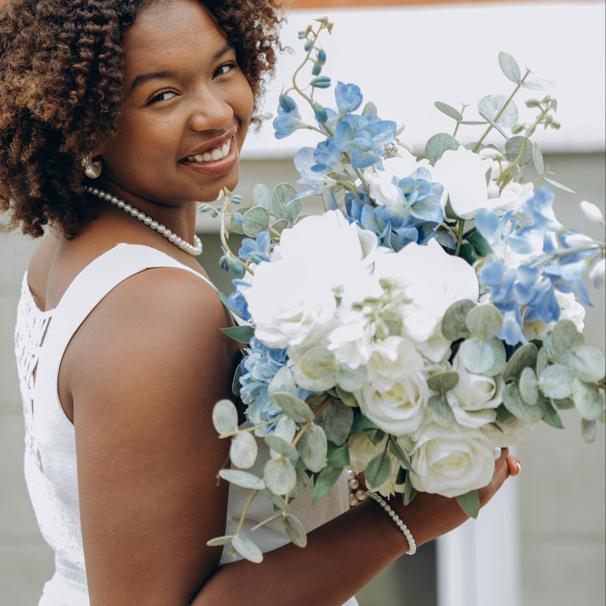 Woman holding a bouquet of flowers in front of a brick wall.