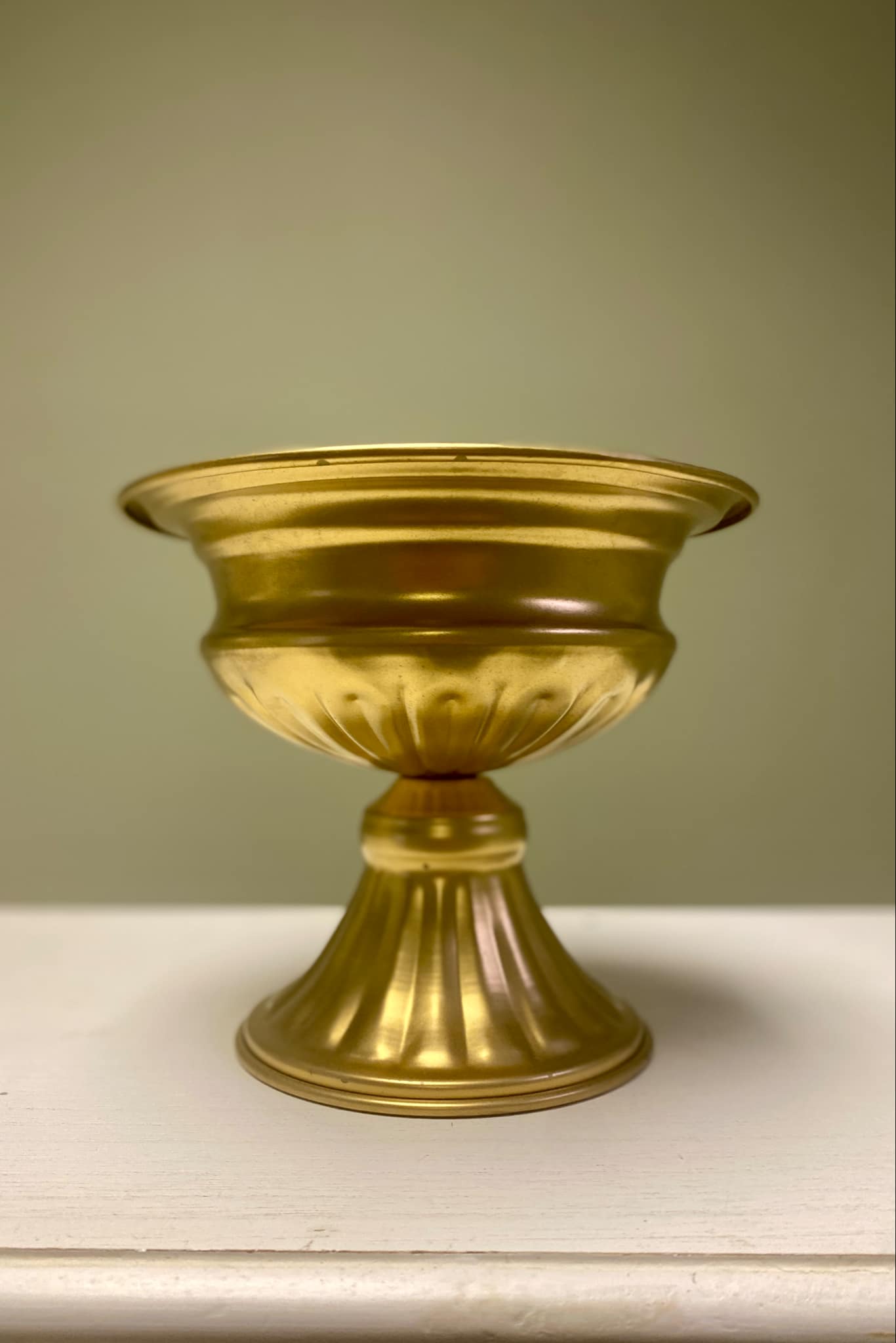 Gold metal pedestal vase on white table 